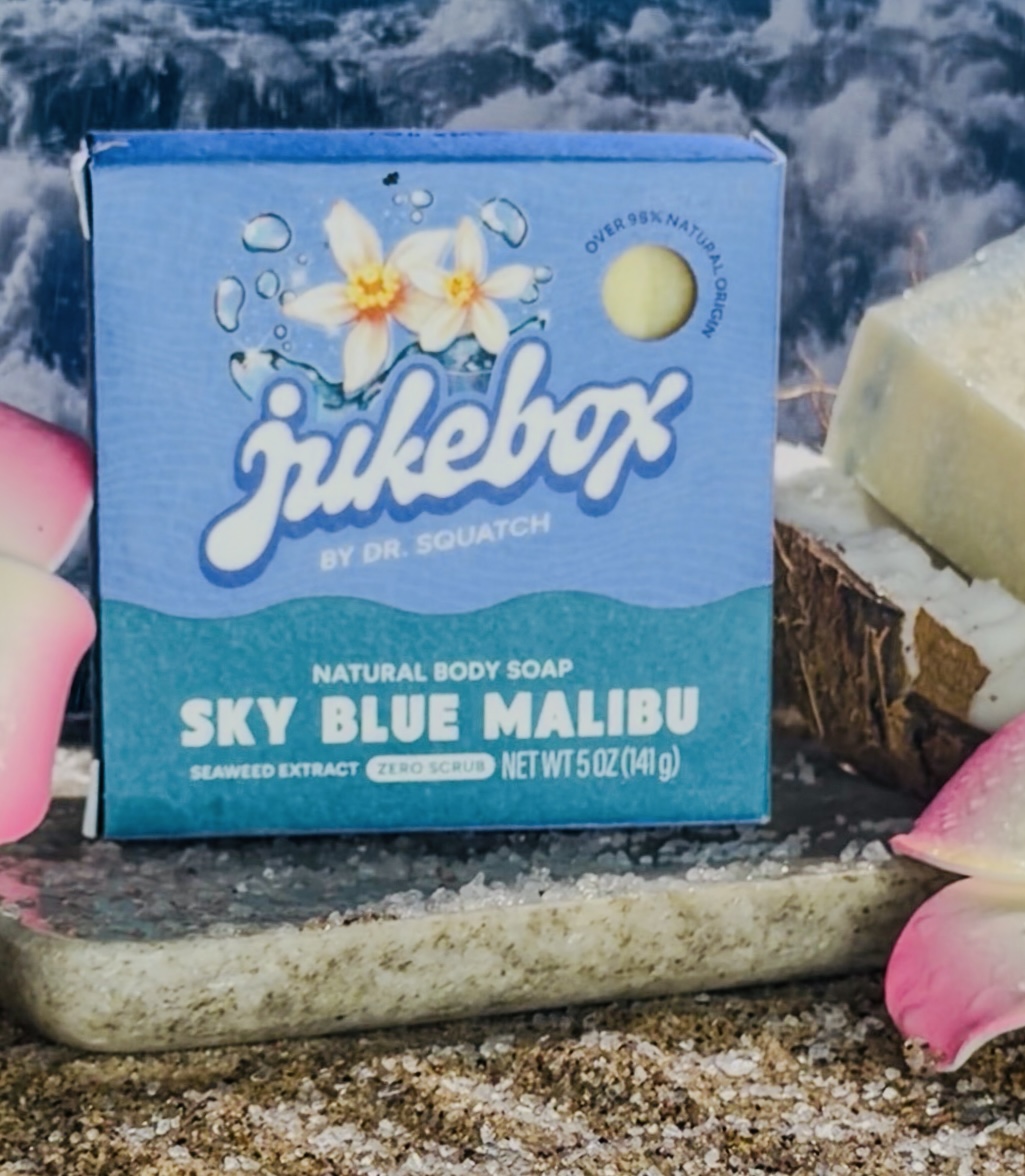 Dr. Squatch Jukebox Sky Blue Malibu soap on a stone tray with coconut, petals and ocean backdrop
